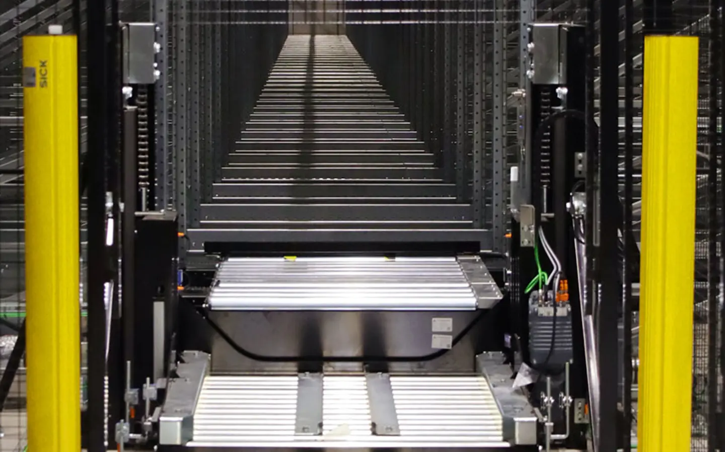 Automated warehouse conveyor system between tall storage racks with yellow safety barriers