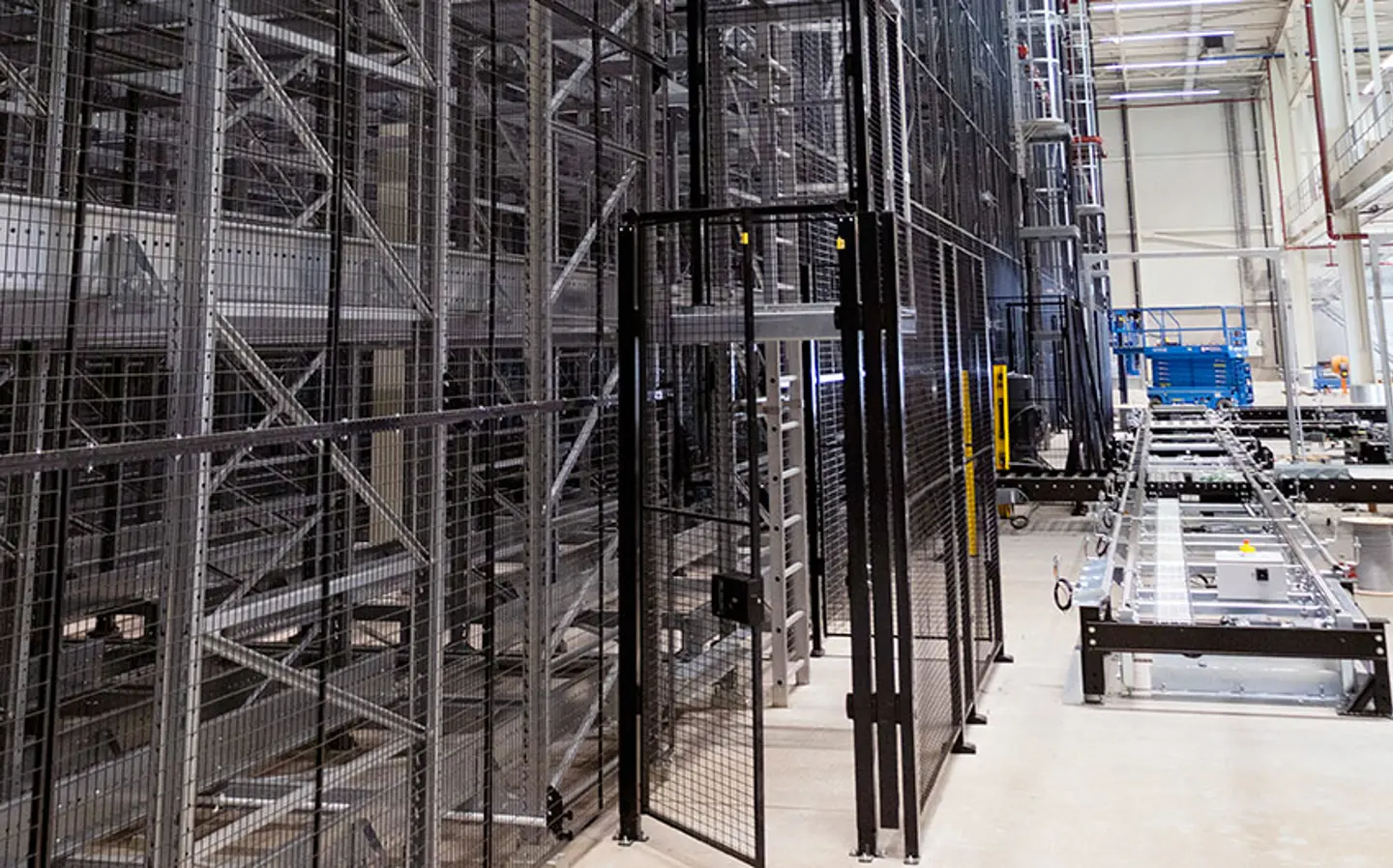 Warehouse with tall storage racks, safety fencing, and conveyor equipment